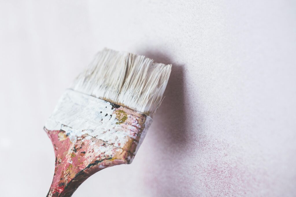 Close-up of a paintbrush applying white paint on a wall, showcasing a minimalist aesthetic.